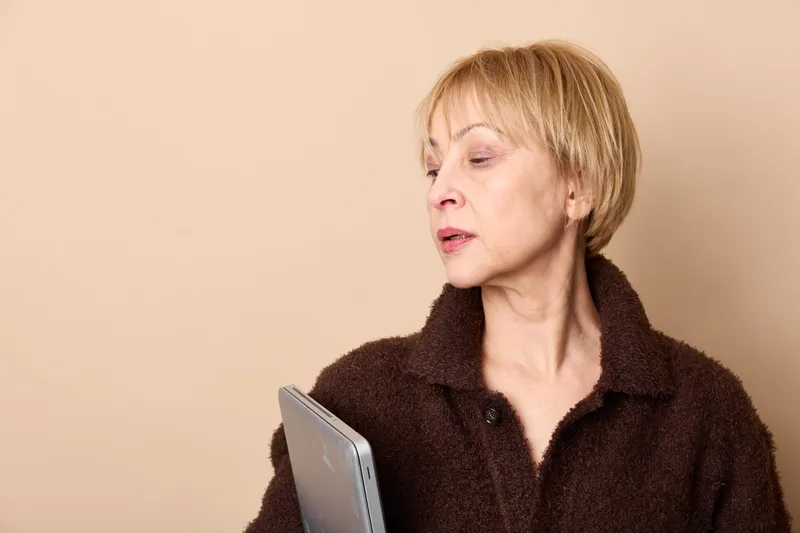 Calm senior woman portrait, short hair holding a tablet, closeup in soft indoor beige light, technology for communication, relaxation, studio background, copyspace