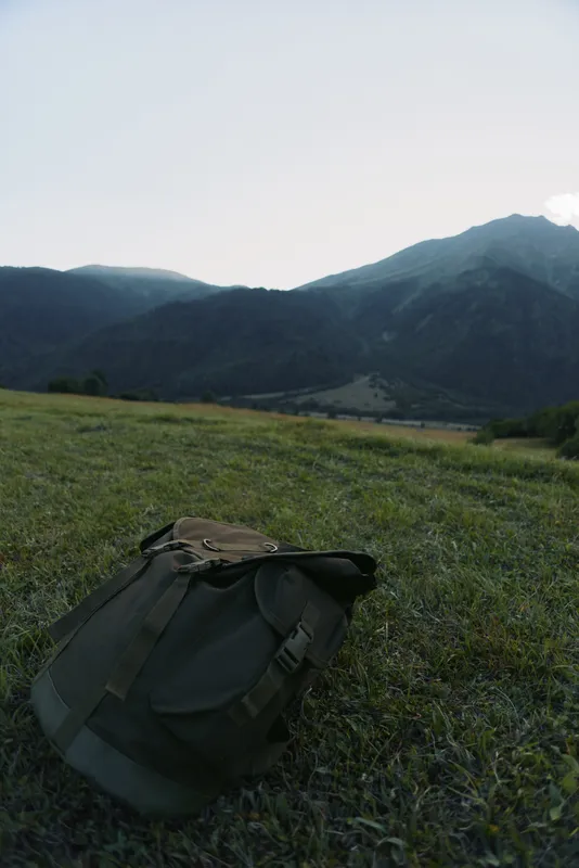 Backpack resting on a grassy meadow with distant mountains under a clear sky. Outdoor lifestyle scene highlighting hiking, nature, exploration, and solitude.