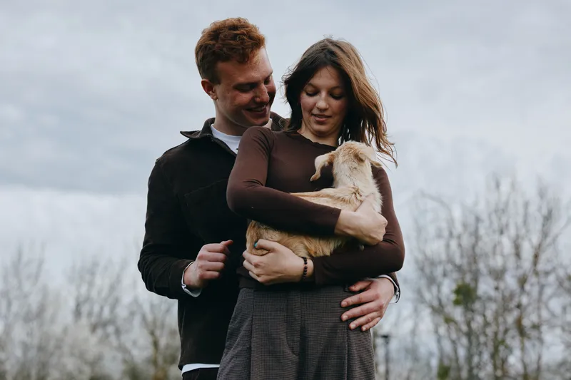 A couple with a goat kid outdoors share a moment of love, affection, and trust in nature. A warm lifestyle portrait highlighting family bonds, tenderness, and connection.