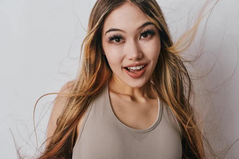 Young woman smiling and posing with long hair flowing, wearing casual sleeveless top, isolated on white background for beauty and lifestyle concept.