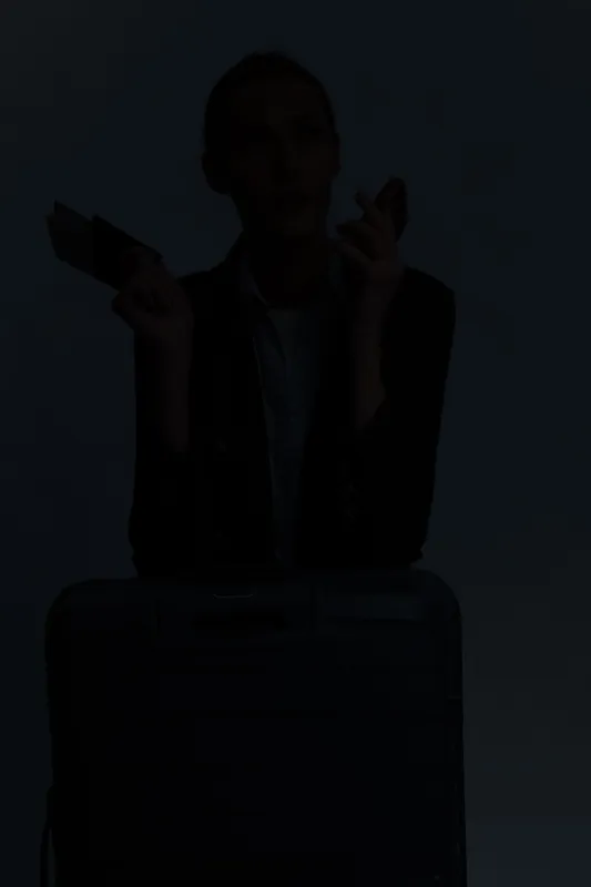 Silhouette of a woman holding credit card and smartphone with suitcase in front. Concept of travel planning, online booking, and modern lifestyle in minimalistic dark setting.