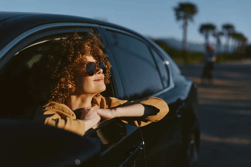 Woman lifestyle car window sunglasses retro film color sunset travel mood, relaxed and confident, inside a sleek automobile during golden hour