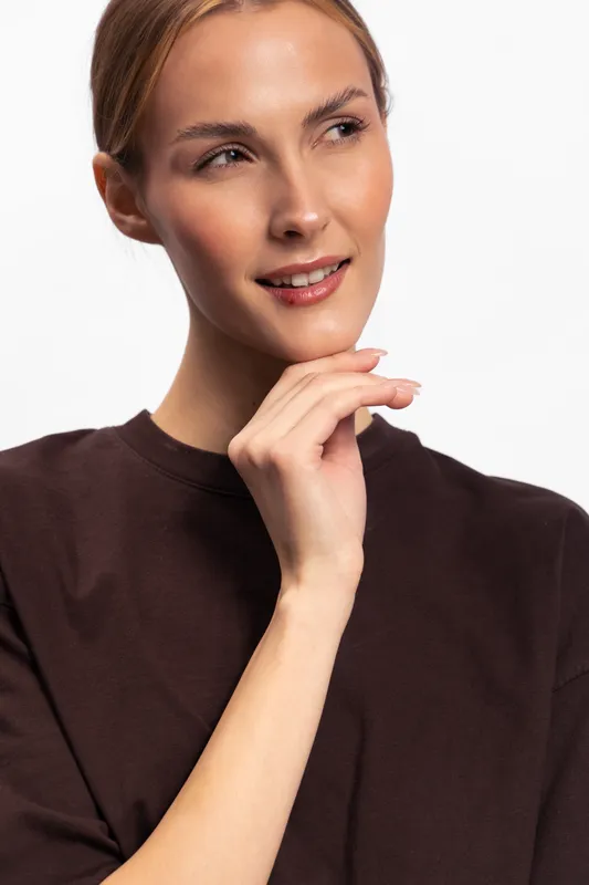 Portrait of a smiling young woman with clear skin and light hair wearing a dark brown top on white background. Concept for beauty, skincare, and natural look.