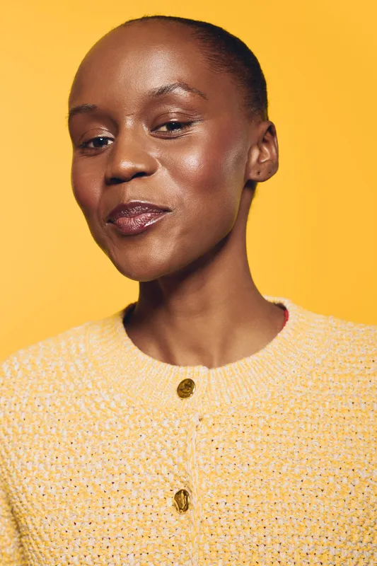 Confident African woman with dark skin wearing a yellow sweater poses against a bright yellow background. The portrait shows natural beauty and stylish casual fashion concept.