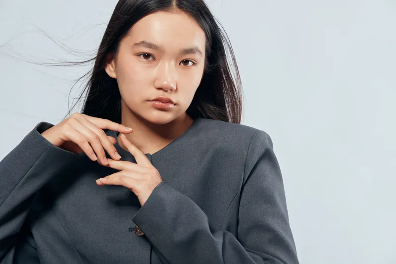 Young woman posing in casual dark blazer with natural makeup and straight hair against light background for fashion and style portrait photography.