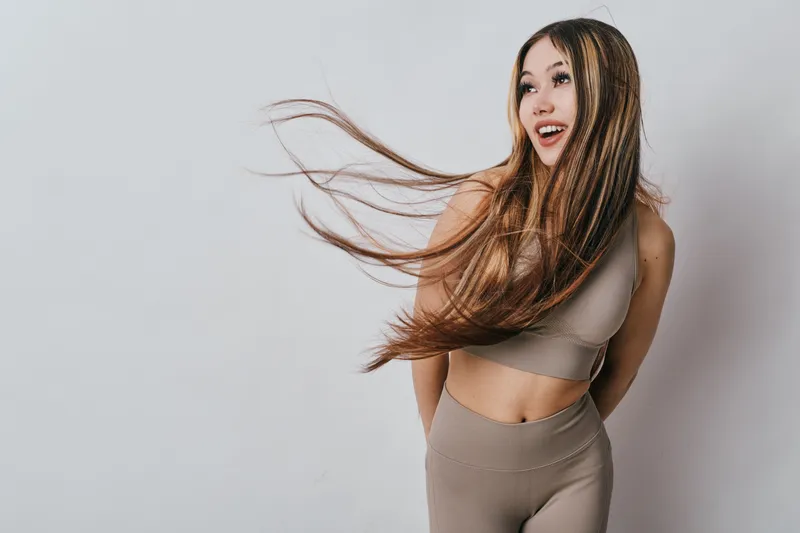 Young woman with long hair wearing sportswear poses on plain background, smiling and looking aside with movement and natural expression for lifestyle and fitness concept.