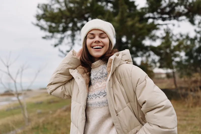 Woman outdoor winter clothing smiling in a beige jacket and beanie enjoying a breezy day in a rural landscape in wide fields with fresh air