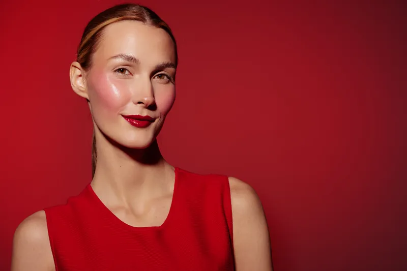 Portrait of confident woman with red lipstick and sleeveless red dress against red background. Concept of beauty, fashion, elegance, and bold makeup in studio lighting.