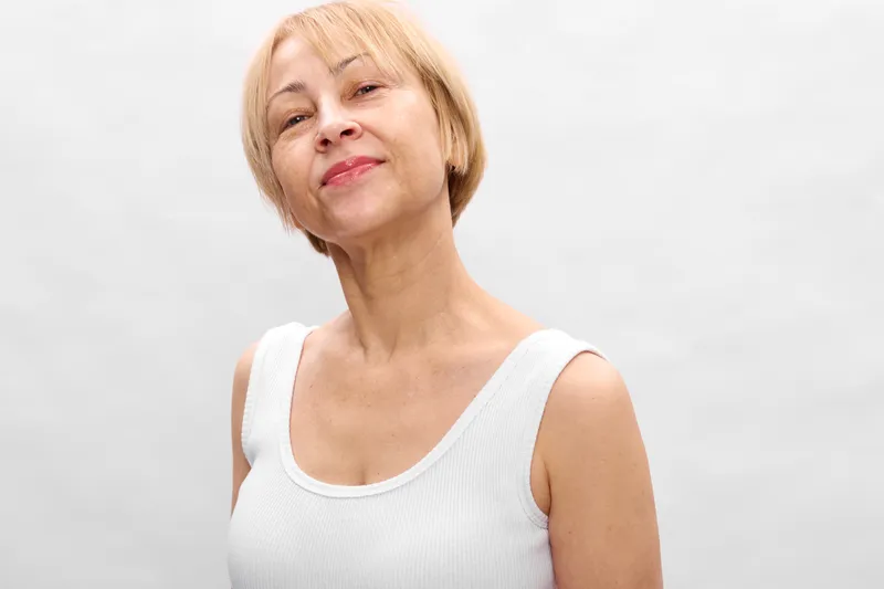 Elderly woman portrait, smiling softly, relaxed posture, studio closeup, white background, calm face, natural skin texture, soft light, subtle gentle shadows
