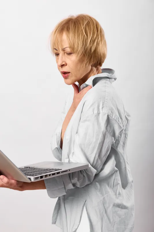 Mature woman with short blond hair working on laptop looks surprised, technology for remote communication, online work, studio portrait, clean white background