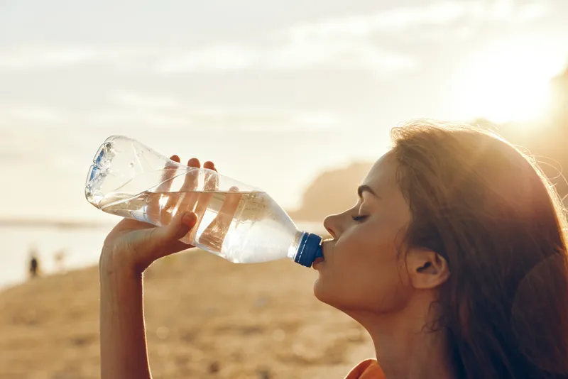 Woman drinking water, hydration and thirst relief concept, outdoors in summer sunlight, close up side view, focused calm expression, healthy wellness lifestyle, active recreation today