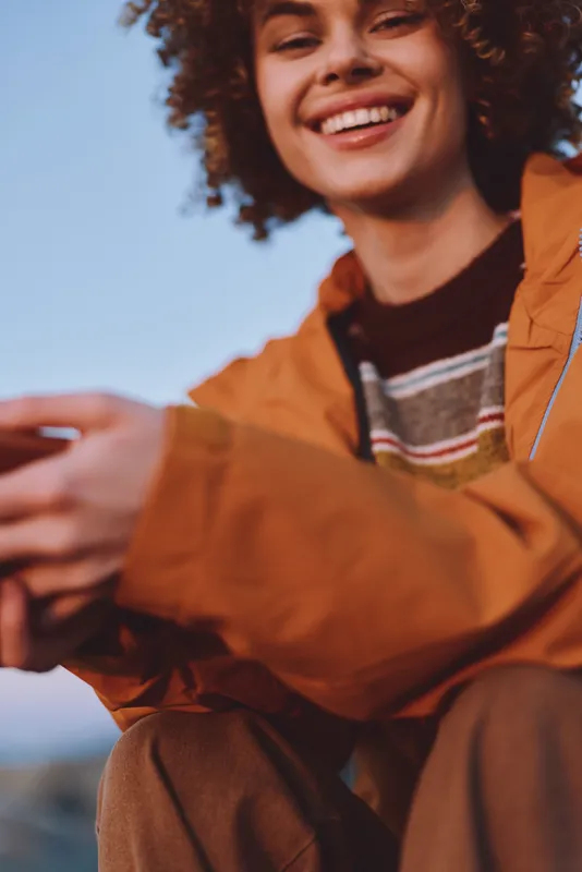 Woman lifestyle outdoors, smiling curly haired young woman in orange jacket, warm sunlight, casual portrait with soft blur, relaxed candid moment, copy space