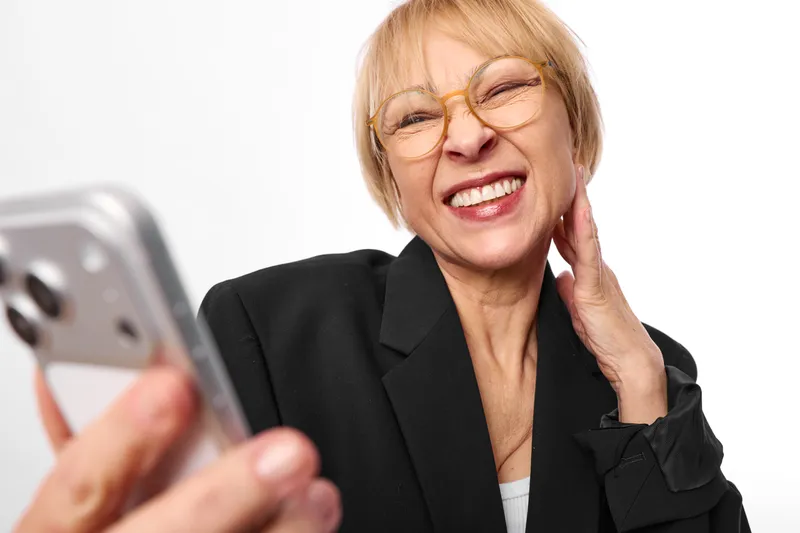 Woman phone smartphone call smile glasses senior business communication portrait, holding smartphone near ear, laughing warmly in office light, looking at screen, confident communication moment,