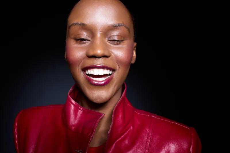 Close-up portrait of a smiling African woman with dark skin wearing a red leather jacket. Her eyes are closed and she shows white teeth. Concept of happiness, beauty, and fashion.