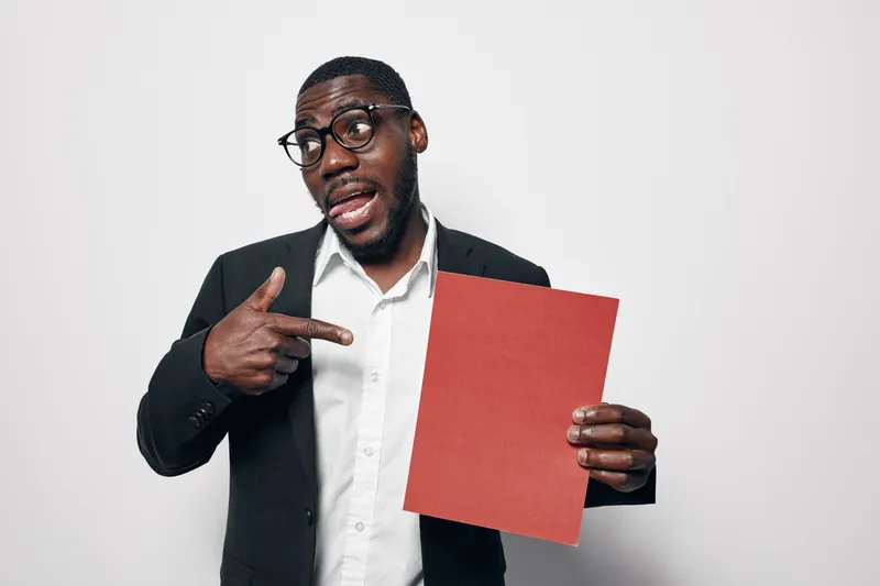 African American man with dark skin wearing glasses and black suit pointing at red paper on white background. Businessman, presentation and communication with confident expression.
