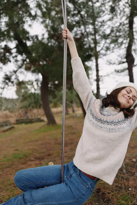 Girl on a swing in a park, wearing a cozy sweater and jeans, enjoying outdoor play and fresh air among trees, capturing a joyful moment outdoors