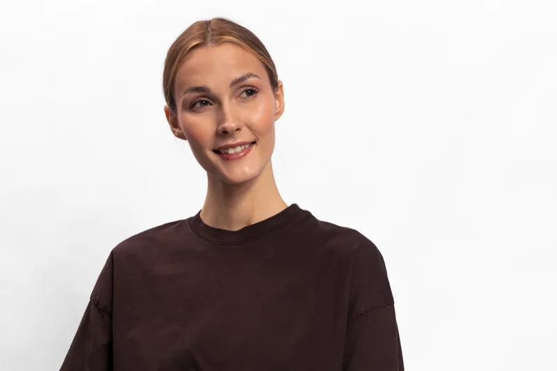 Young woman with fair skin and light brown hair smiles gently wearing a dark brown shirt against a white background. Concept of casual style, happiness, and natural beauty.