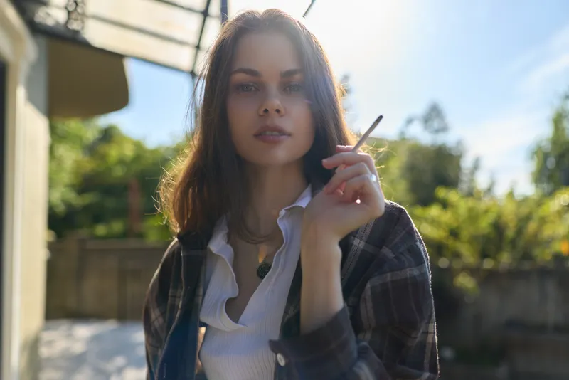Cheerful woman outdoors, casual lifestyle portrait in sunlight with breeze, relaxed pose, natural colors and plaid shirt, candid mood in a sunny urban garden backdrop