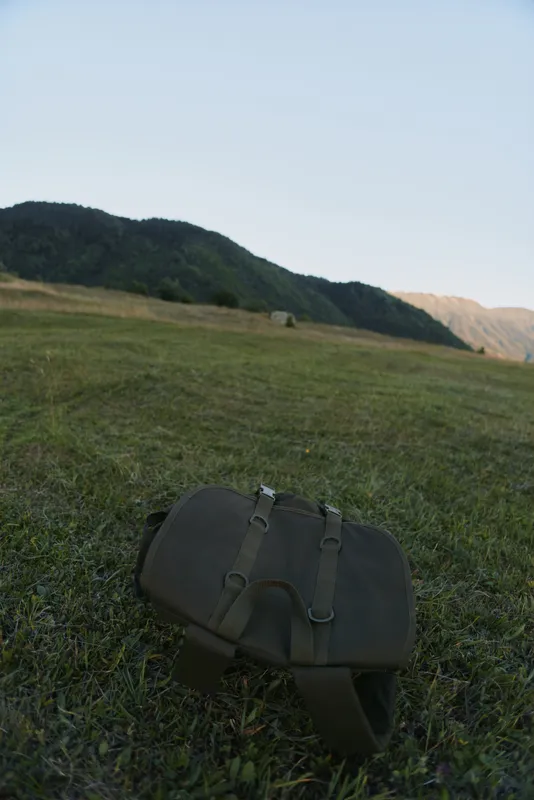 Brown shoulder bag on a grassy field with rolling hills in the distance, an outdoors lifestyle moment focused on travel and preparation.