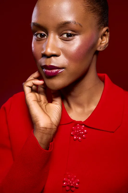 Portrait of confident black African woman with dark skin wearing red coat with flower buttons on red background. Concept of fashion, beauty, elegance, and strong female model.