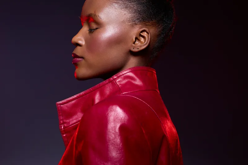 Profile of a dark skinned African woman with closed eyes wearing a red leather jacket. Studio portrait with dramatic lighting highlights her smooth skin and confident expression.