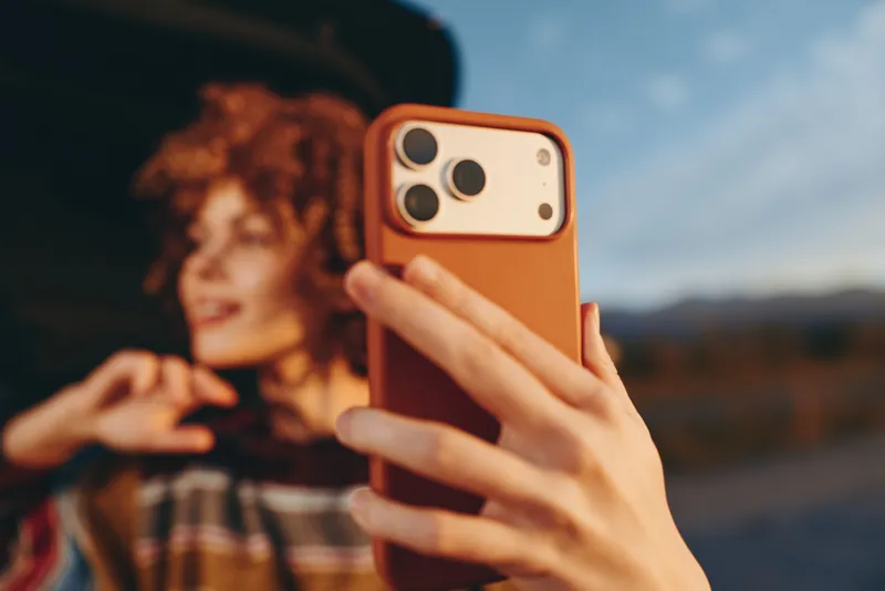 Woman lifestyle selfie smartphone outdoors portrait, hand closeup holding phone, blurred background of woman on street, casual travel moment, soft natural light evening, shallow depth of field.