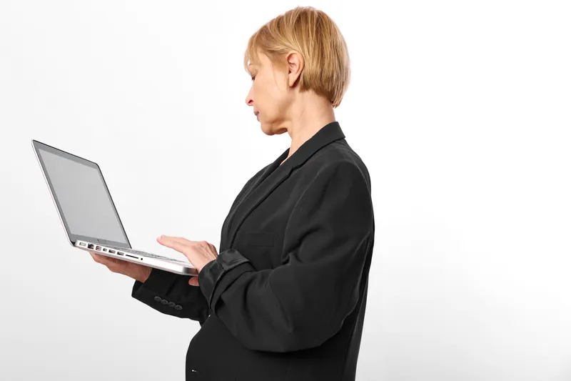 Woman with short hair holding a laptop, side profile, typing in studio on white background, business work concept, remote technology support, clean minimal scene