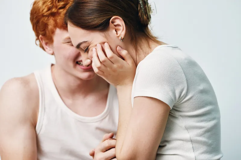 Young couple laughing and smiling together in casual clothes, close up portrait with white background and intimate joyful moment between friends.