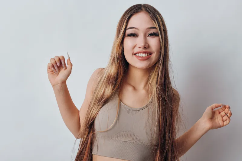 Young woman smiling and dancing with long hair in casual top on light background. Happiness, movement, beauty and lifestyle with cheerful female expression.