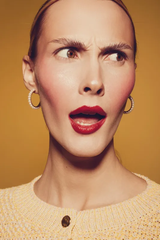 Close-up of surprised woman with red lipstick and hoop earrings looking sideways on yellow background. Concept of emotion, reaction, beauty, and fashion portrait.