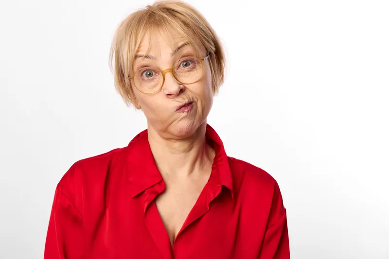 Woman elderly glasses surprised portrait red shirt white background studio indoor closeup headshot puckered lips astonished expression looking at camera clean minimalist space