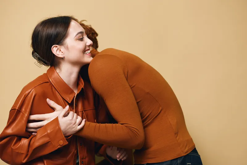 Couple embracing in warm clothing with smile, showing affection and emotional connection in simple studio setting with beige background and casual fashion style for friendship or love.