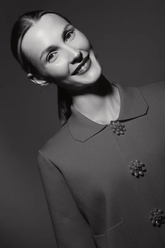 Smiling caucasian woman with fair skin in vintage style coat poses on dark background. Concept of retro fashion, beauty, and elegance.