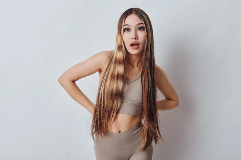 Young woman with long hair in crop top and leggings posing with surprised expression against white background in studio. Fitness, model, casual outfit and emotion captured.