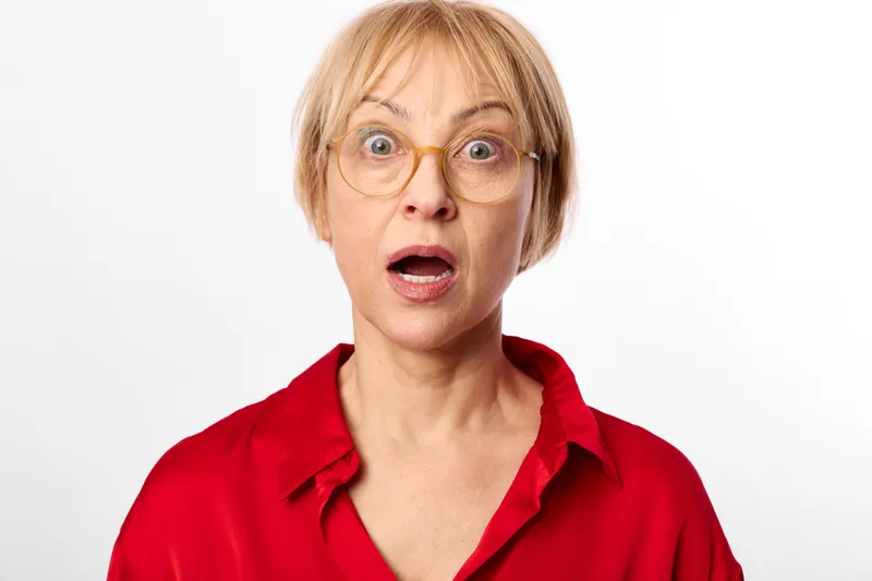 Surprised woman with round glasses, red shirt studio portrait on white background, close face framing, expressive eyes, short haircut, bright neutral lighting, minimal clean look