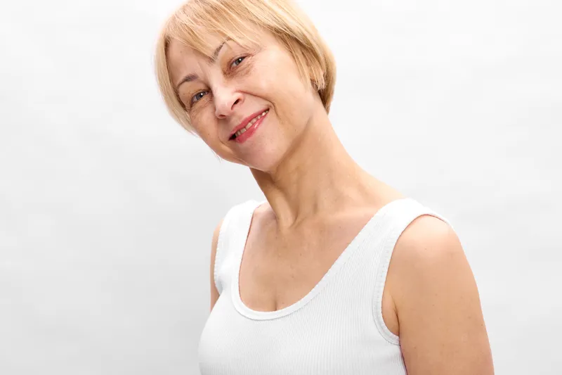 Woman senior blonde portrait closeup in white studio background, calm expression, white tank top, skincare routine, wellness and self care concept, soft studio light