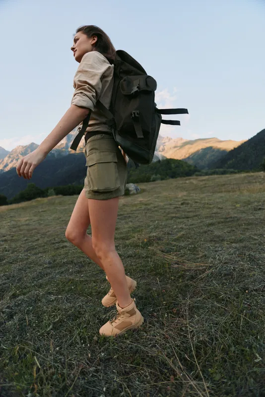 Woman hiking along a mountain trail with a backpack in a grassy alpine landscape, conveying active lifestyle and lone exploration in nature