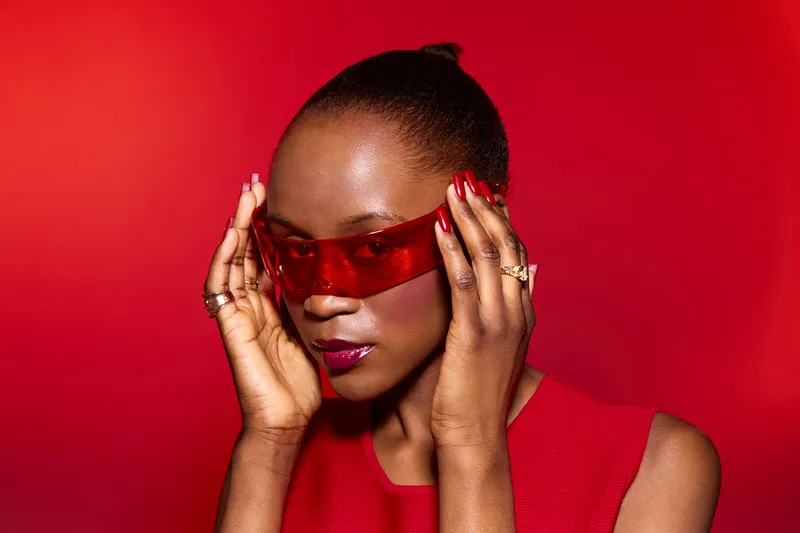 Stylish dark skinned African American woman wearing red sleeveless top and red sunglasses poses on red background. Concept of fashion, beauty, style, and confident female model.
