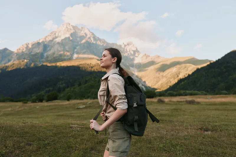 Young woman with a backpack hikes through a mountain meadow enjoying the fresh air and scenic views during a sunny day outdoors.