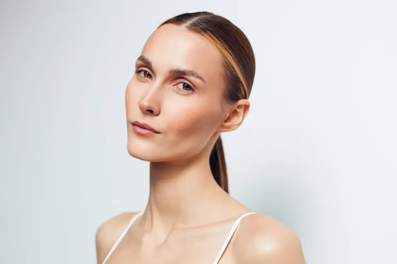 Close-up portrait of a calm woman with clear skin and subtle makeup, facing slightly to the side in soft studio light. Concept: serene beauty and minimal skincare.