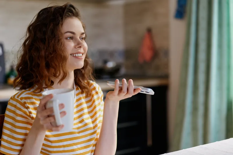 Happy woman in a yellow striped shirt enjoys coffee at home, smiles while holding a mug, relaxed kitchen scene, candid lifestyle moment, warm natural light, cozy morning and serenity