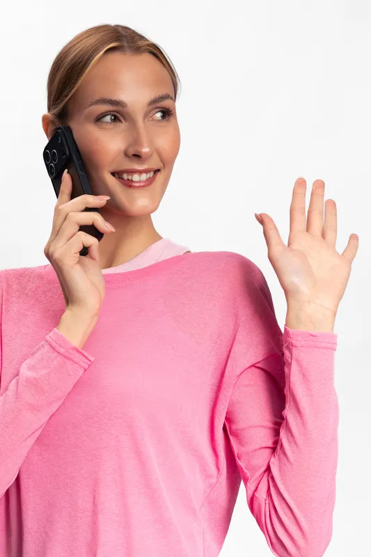 Young woman in pink sweater smiling and talking on smartphone while waving hand isolated on white background. Concept of communication, greeting, and casual lifestyle.