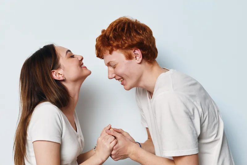 Young man and woman holding hands and smiling with happiness and love in casual clothes on plain background. Couple bonding and joyful interaction in relationship moment.
