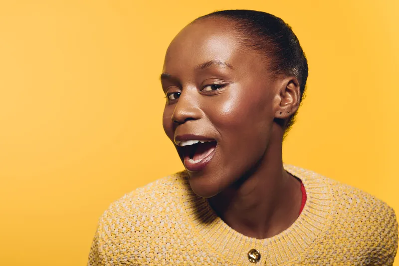 Happy African woman with dark skin and natural hair smiling confidently, wearing a yellow sweater against a bright yellow background. Concept of joy, beauty, and positivity.