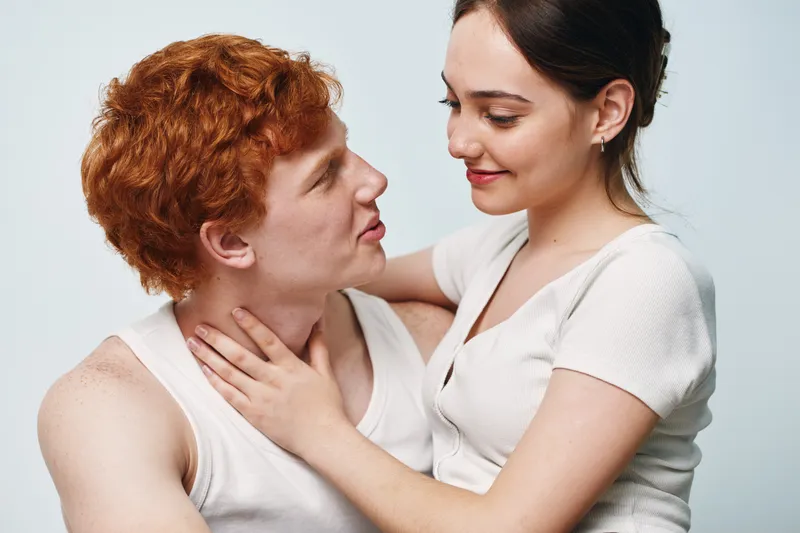 Young couple embracing and looking at each other with affection against white background. Romantic moment with man and woman in casual clothes expressing love and connection.