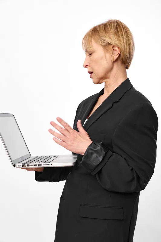 Businesswoman with laptop in studio, professional woman in black blazer, concerned face, stopping gesture, looking at keyboard, white background isolated