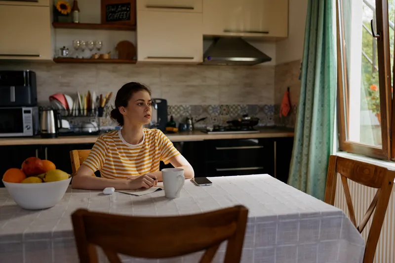 Candid woman at a kitchen table, morning light, relaxed pose, sipping coffee, fruit bowl nearby, striped shirt, home lifestyle scene