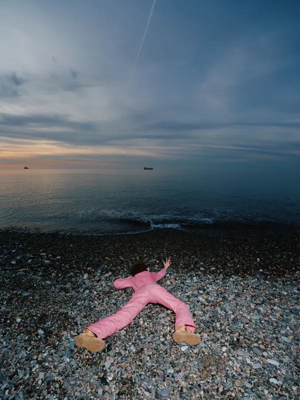 Beach scene with a pink plush toy lying on pebbles as waves meet the shore at dusk, calm sky and distant boat on the horizon for a tranquil coastal moment
