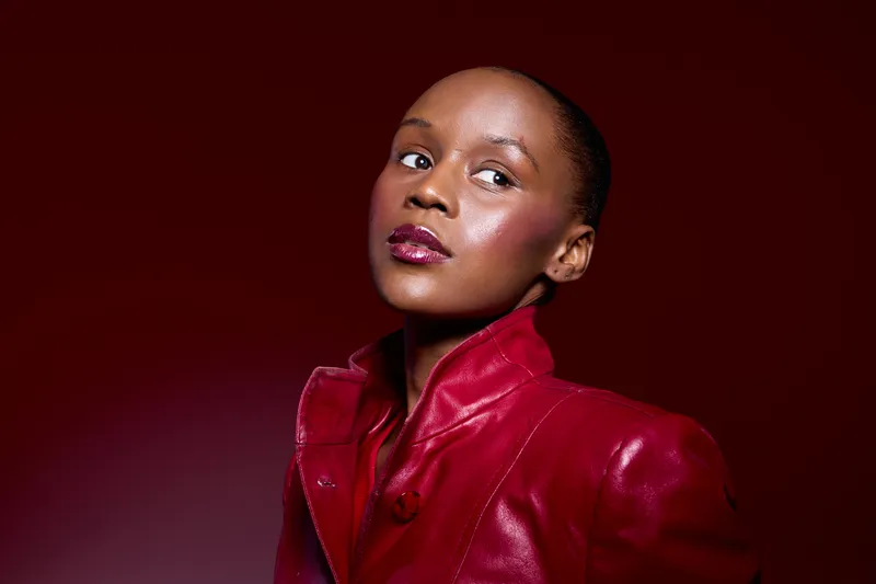 Portrait of confident dark skinned African American woman wearing red leather jacket on red background. Studio lighting highlights her glossy lips and smooth skin. Fashion concept.