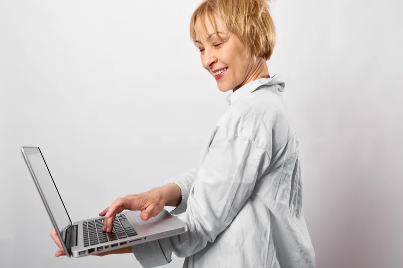 Woman, laptop, typing, senior, smile, online, work, home, technology, portrait, profile on white background, calm expression, casual clothing, focused screen